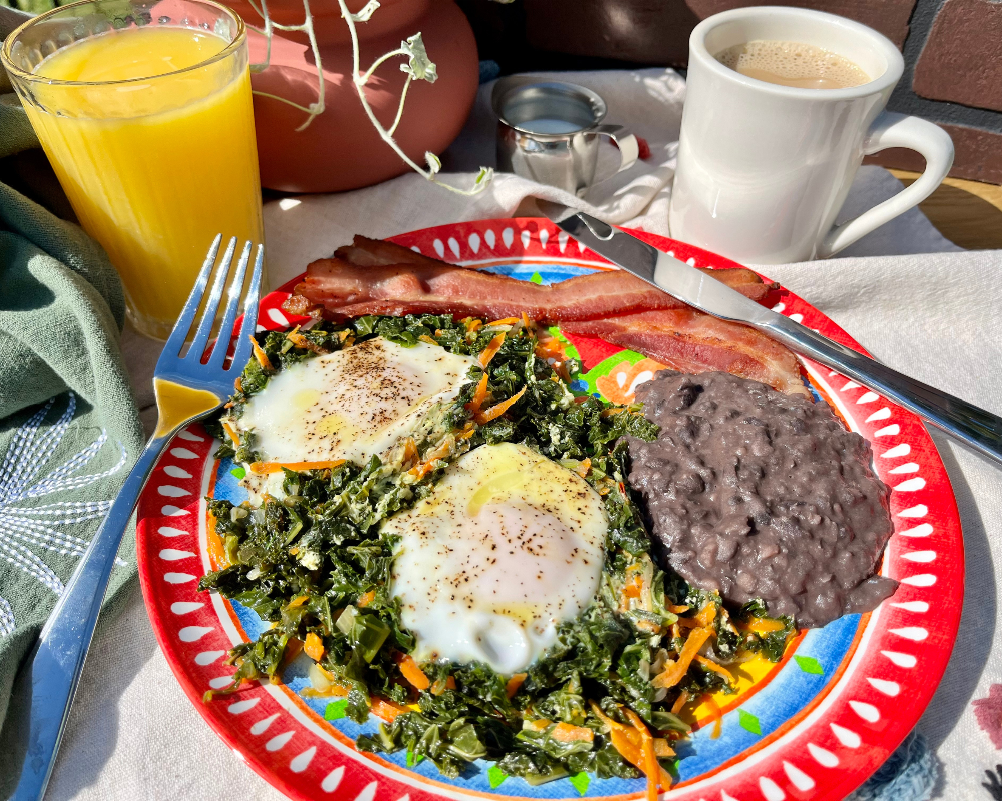 Eggs in a nest breakfast, 2 sunny side eggs on top of kale and carrots, side of beans and meat bacon or sausage